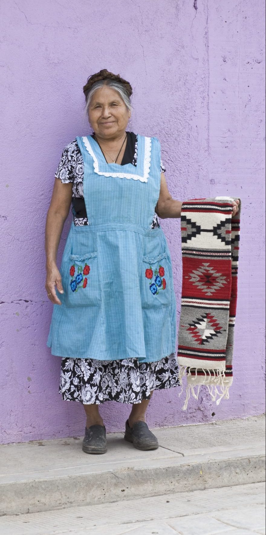Friendly, smiling local indigenous Mexican woman vendor displaying handwoven Zapotec rug outside shop, Santa Ana del Valle, Oaxaca, Mexico