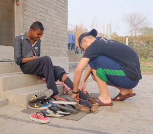 Man helps orphan child put clean socks and shoes on.